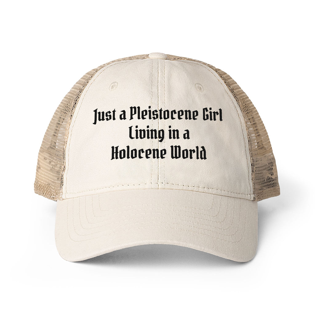 A beige trucker hat with a cream front panel and tan mesh back, featuring the text 'Just a Pleistocene Girl Living in a Holocene World' printed in black on the front.